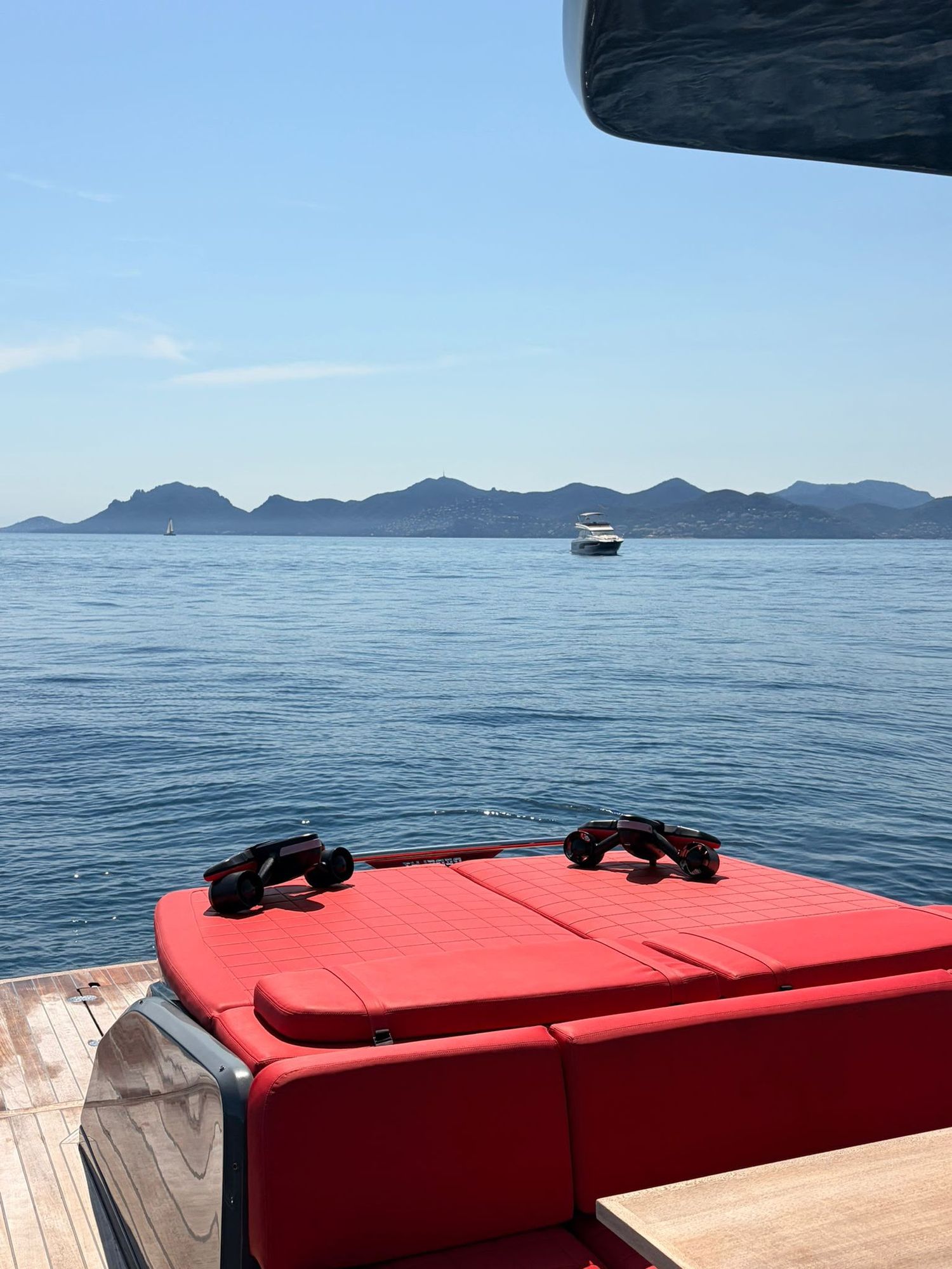 The aft sunbed with sunglasses left on it, open water and the red Estérel hills beyond