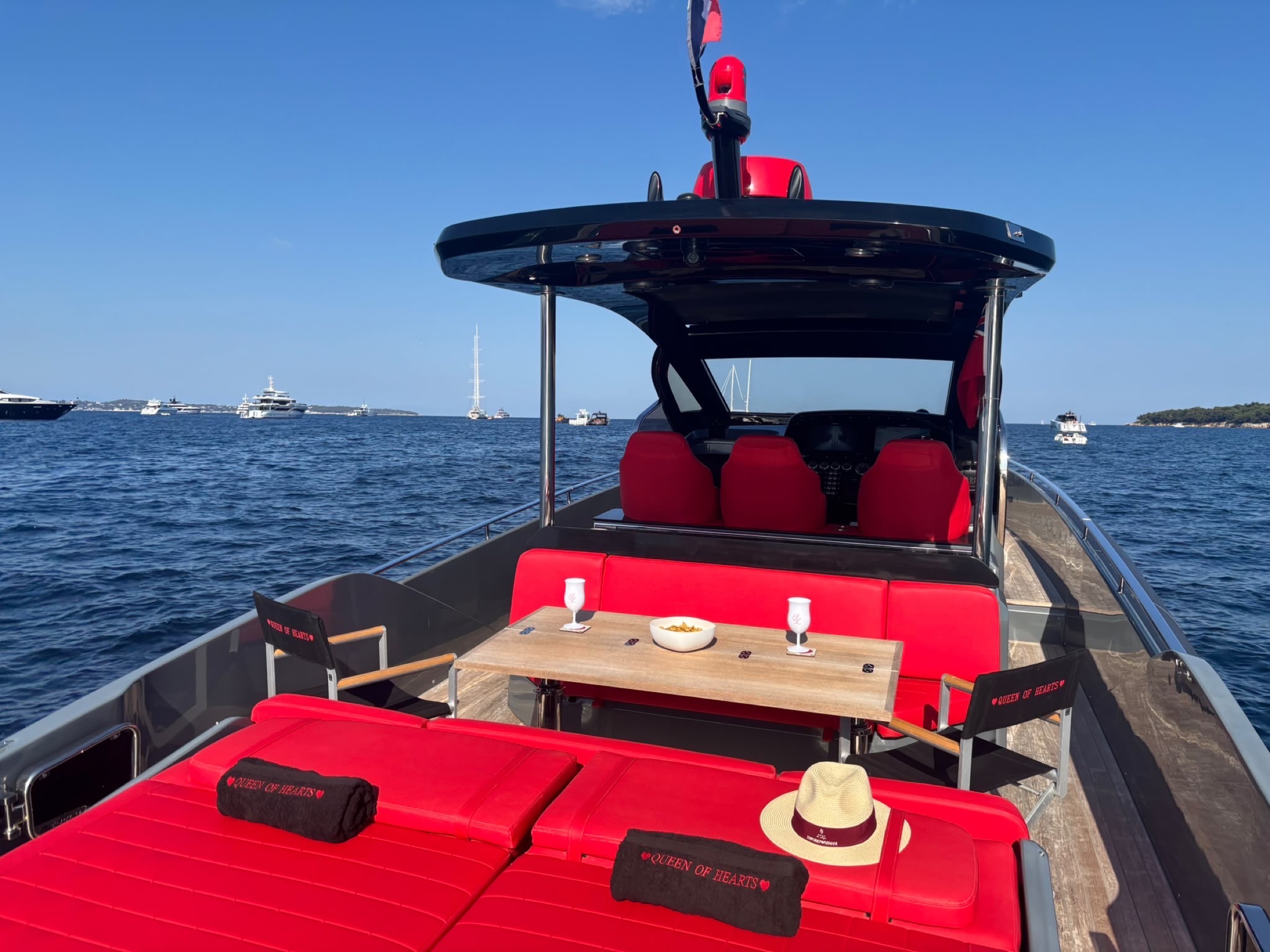 The aft deck set for the day — table, hat and towels on the red sunbeds, the coast beyond